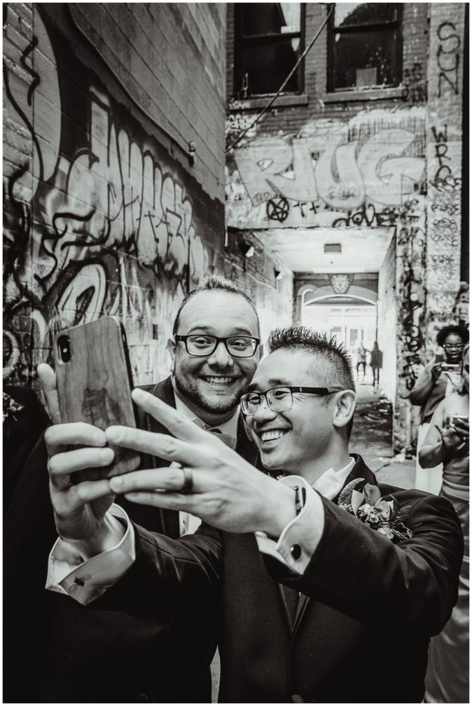 An LGBTQ couple taking a selfies on their wedding day in graffiti alley Ann Arbor Michigan