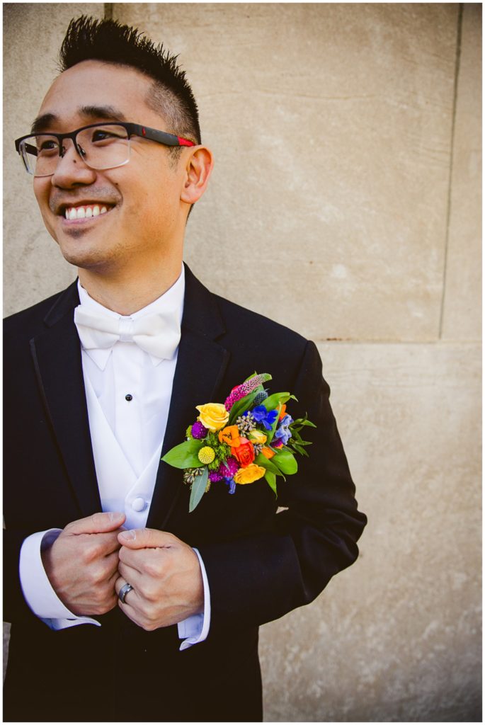 Groom looking off at his husband smiling while the photo is a close up of his pocket floral from University Flower Shop