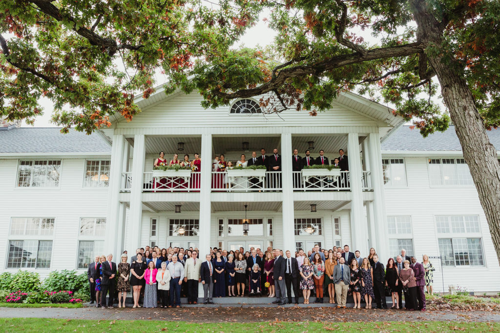 An entire wedding including guests standing outside of the Waldenwoods Lodge in Howell Michigan. Cut your guest list
