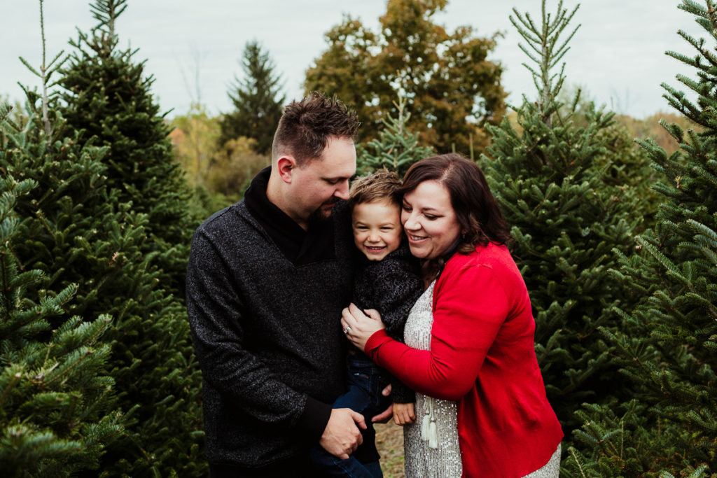 Parents snuggling their son at a Christmas Tree farm for family holiday photos. 10 tips for choosing outfits for your family session