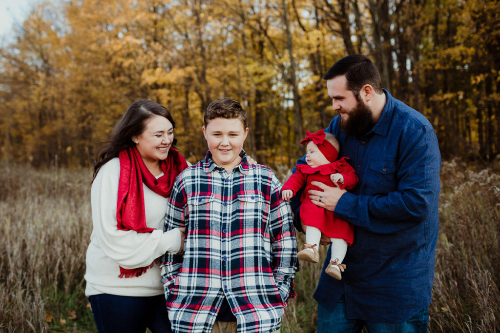 Parents looking at kids in a field in the fall wearing red, blue & some pattern showing 10 tips for choosing outfits for your family session