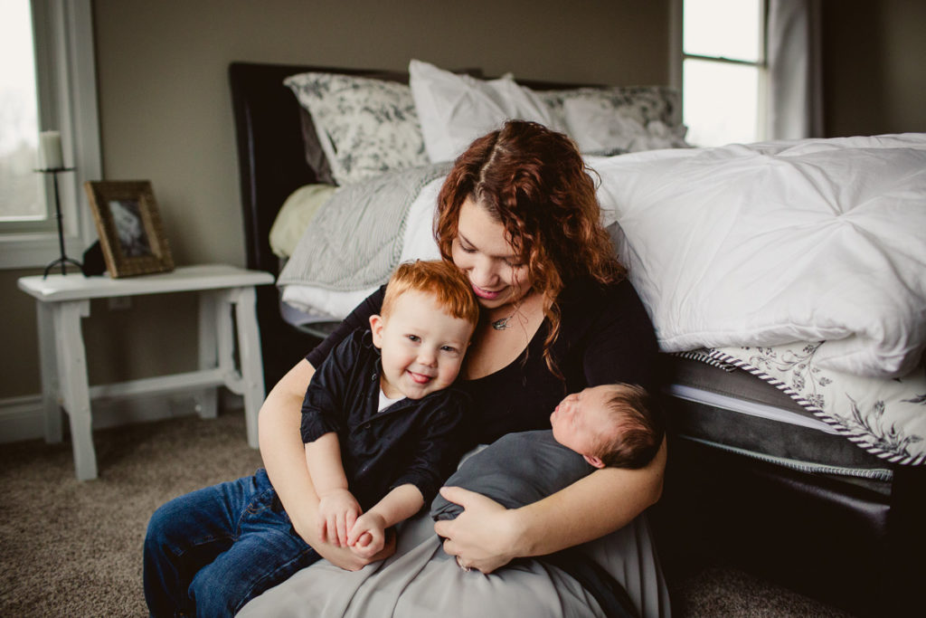 Mother holding her newborn & her older son. SMP guide to your at home newborn session