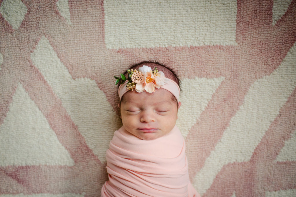 Newborn girl laying on the rug in her bedroom in a pink swaddle & headband. SMP guide to your at home newborn session.