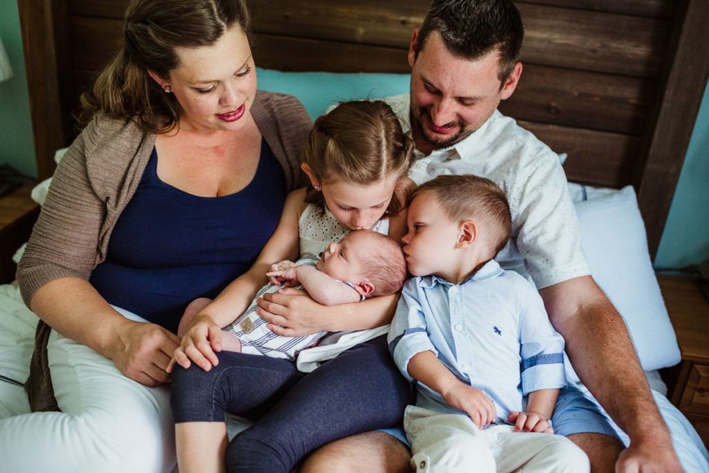 A family of five sitting on a bed together cuddling their newborn baby. What to wear to your newborn session.