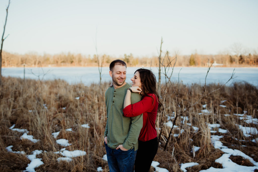 A couple looking at each other in a field of snow and a lake behind them. 8 engagement session prep tips.