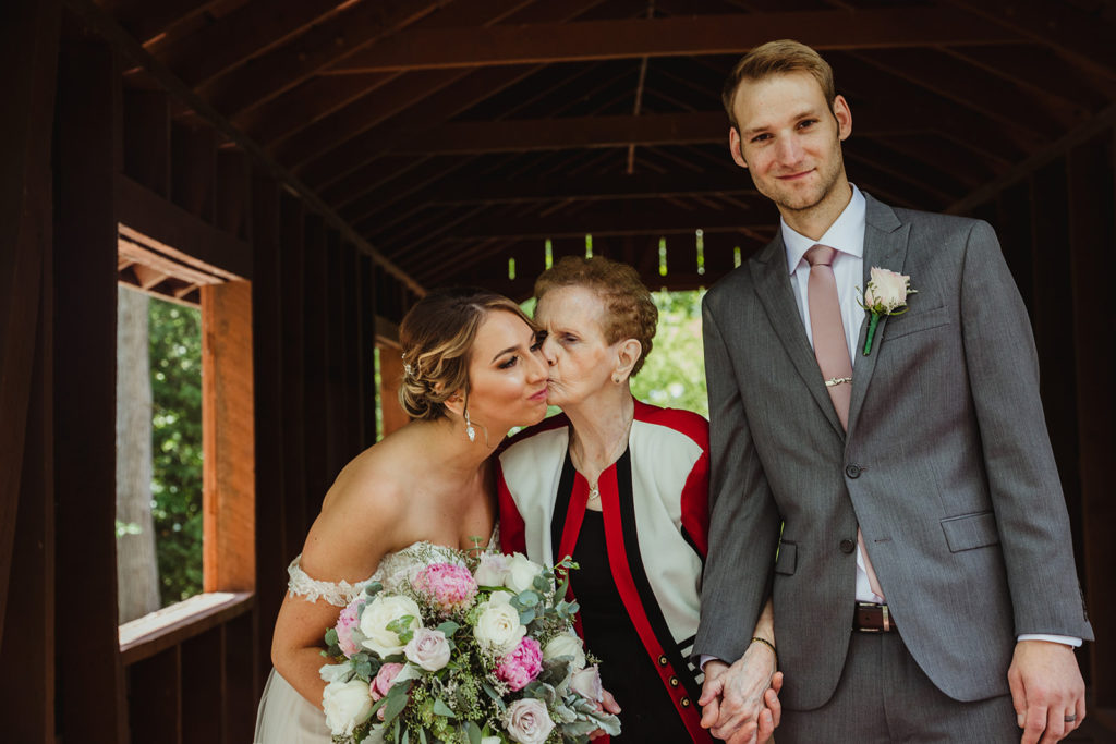 Couple during family photos with Grandma in the middle who is kissing bride on the cheek. Family photos on your wedding day.