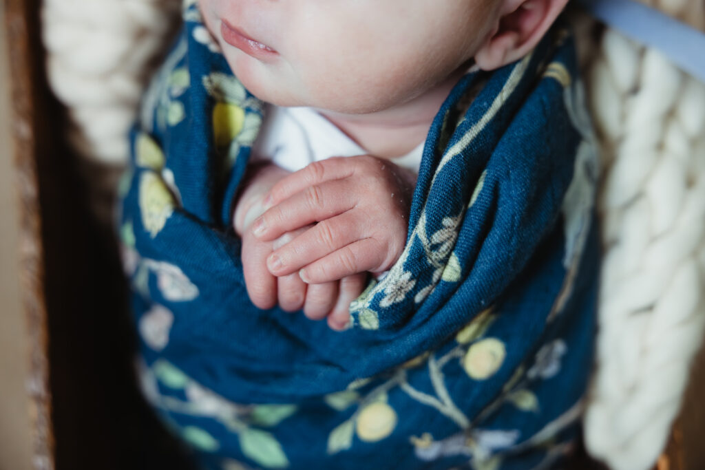 Close-up of newborn baby hands wrapped in a blue swaddle during an in-home Michigan newborn session