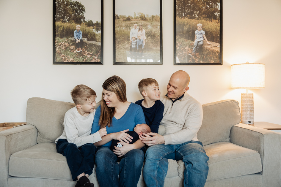 Parents snuggling on their couch holding their newborn and laughing together during an in-home session