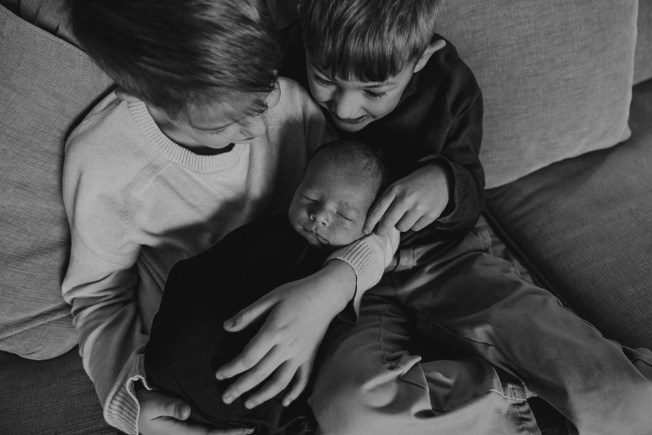 Older brothers snuggling their newborn sibling on the couch during a relaxed lifestyle session